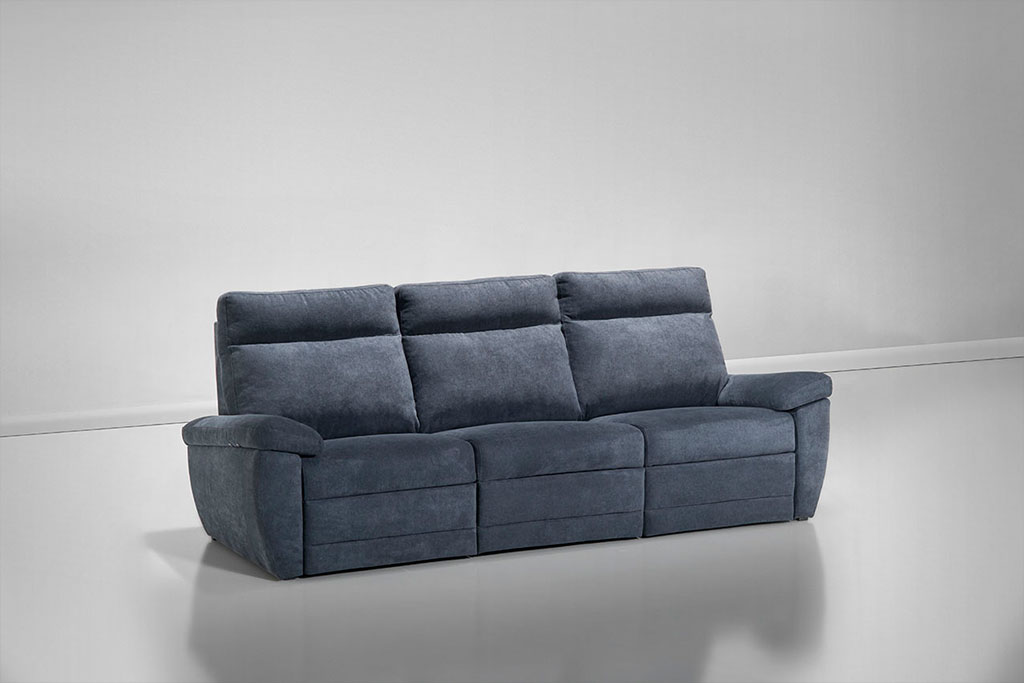 A imagem mostra um ambiente claro no qual há um sofá azul marinho de três lugares. Ele está posicionado na diagonal.