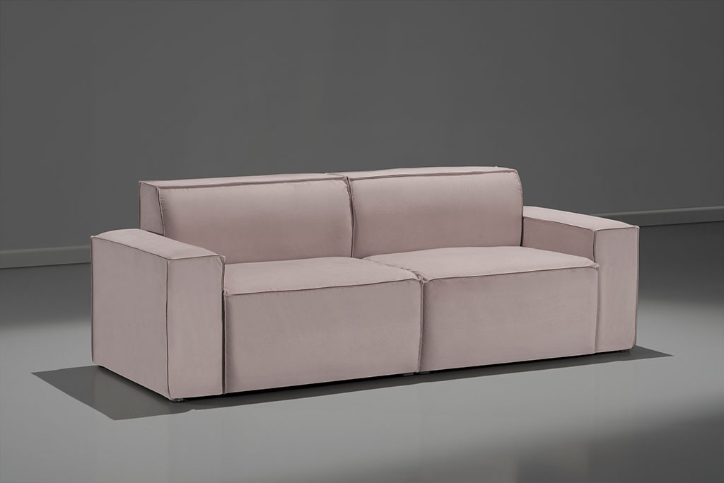 A imagem mostra um espaço escuro, com parede cinza e o piso mais claro, refletindo o sofá. No centro da imagem está o sofá Hermes, na cor marrom.