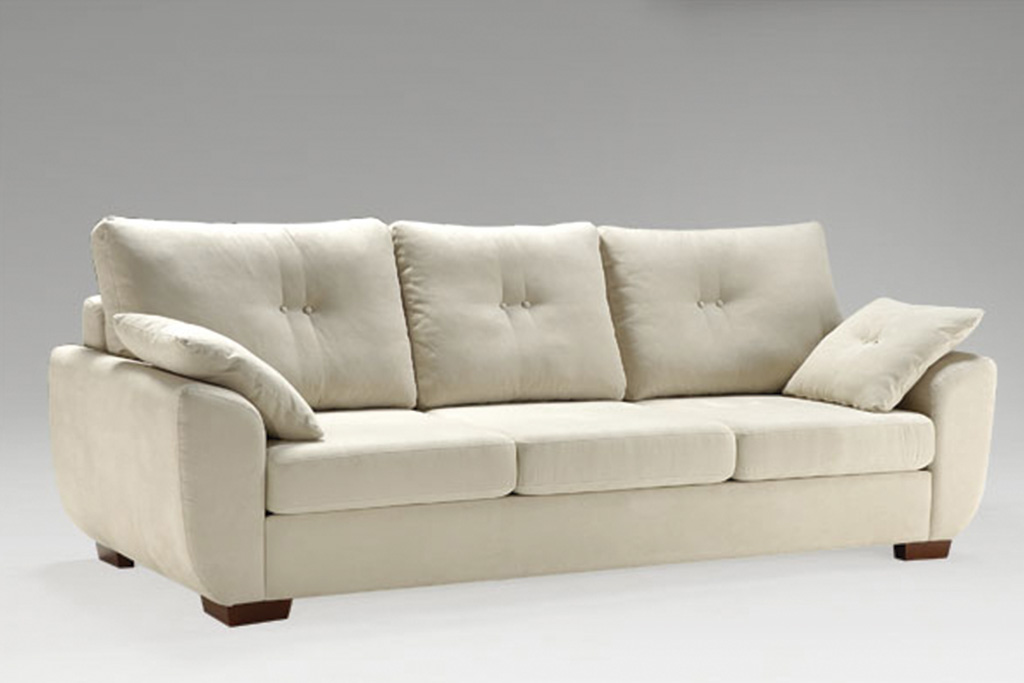 A imagem mostra um ambiente com fundo degradê branco e cinza. No centro encontra-se o Sofá Piaceri, na cor branca com pés de madeira nos cantos do sofá. Há pequenas almofadas, uma em cada canto do sofá.